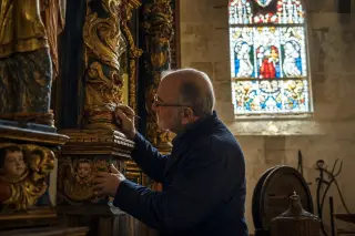 Artisan restoring ornate baroque altarpiece inside a Norman church, with vineyard tools in the background and soft daylight illuminating the scene.